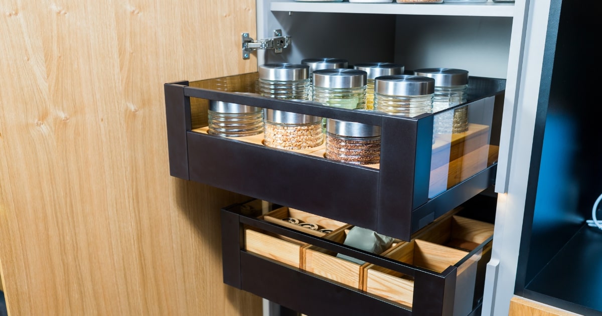 Close-up of a modern kitchen pull-out drawer system with glass jars containing various grains and spices, neatly organised on two levels.