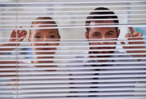 Blinds 5 A man and a woman are peering through partially opened window blinds, creating a sense of curiosity or intrigue. They are standing close together, with both looking intently outside. The blinds create horizontal lines across their faces, adding an element of suspense. The background is out of focus, keeping the attention on the expressions of the two individuals.